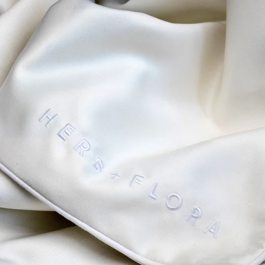 Close-up of the Morpheus Pillowcase satin fabric with embroidered Herb + Flora logo